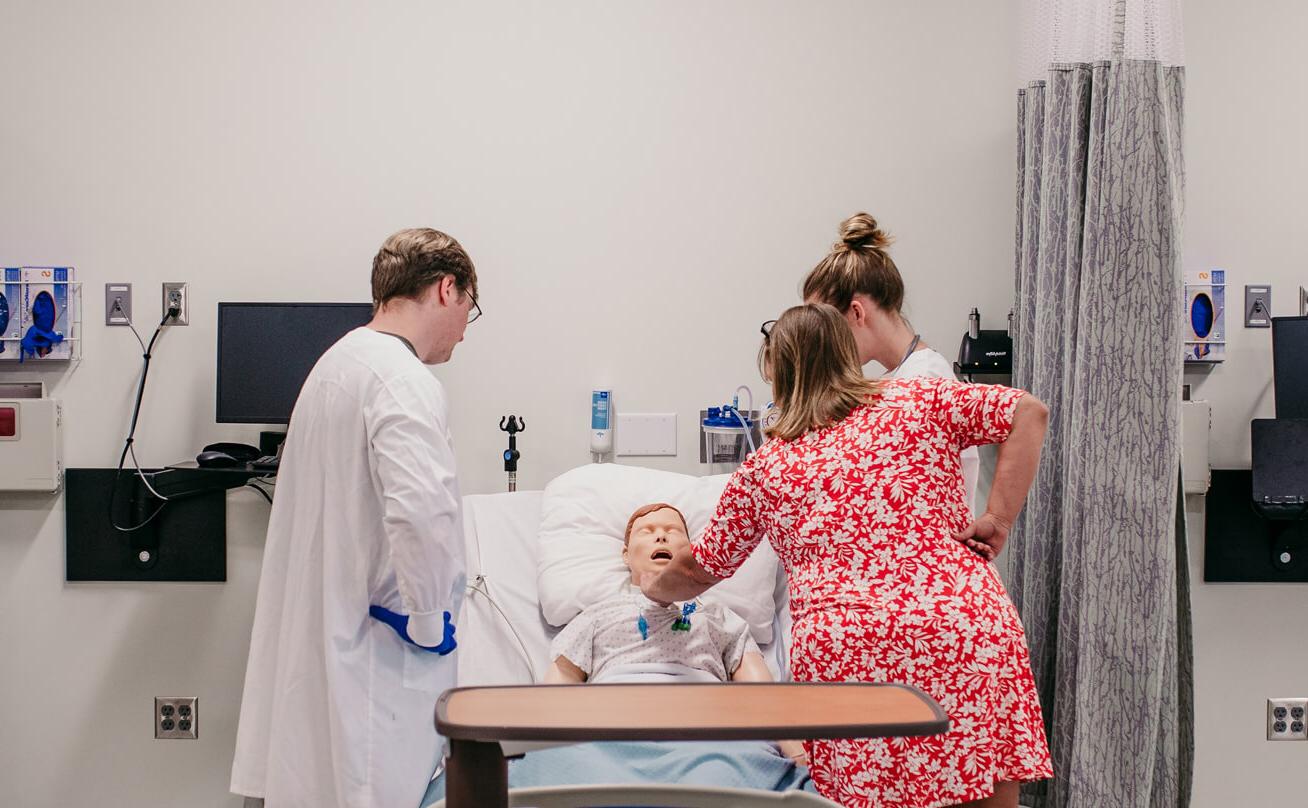 Professor works with students on nursing manikin